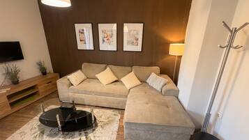 A living room with a sectional sofa, a coffee table, a TV, and framed artwork on the wall.