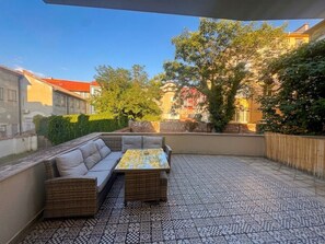 Un patio al aire libre con un conjunto de sofá y una mesa, rodeado de pisos con diseños y vistas a edificios y árboles.
