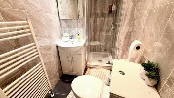A bathroom with a toilet, sink, shower, and a towel rack.