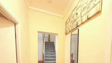 A hallway with a wooden floor, a rug, a staircase, and a wall-mounted mirror.