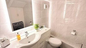 Ein modernes Badezimmer mit einem weißen Waschtisch, einem Waschbecken, einem Spiegel, einer Toilette und einer Duschkabine.