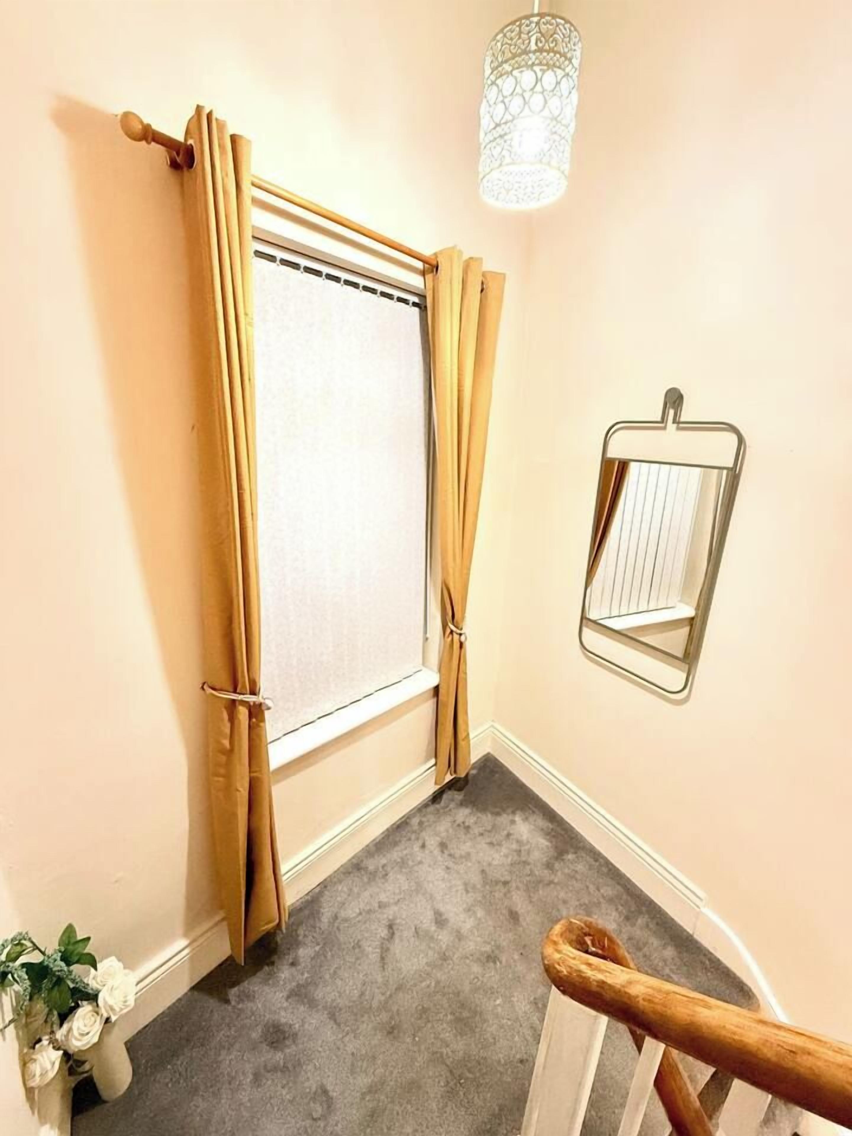 Une pièce d’angle avec une fenêtre, un miroir et un escalier.