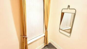 Une pièce d’angle avec une fenêtre, un miroir et un escalier.