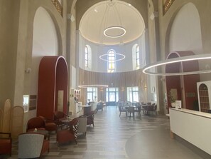 Eine geräumige Lobby mit hohen Decken, Rundbogenfenstern und einem zentralen Empfangsbereich.