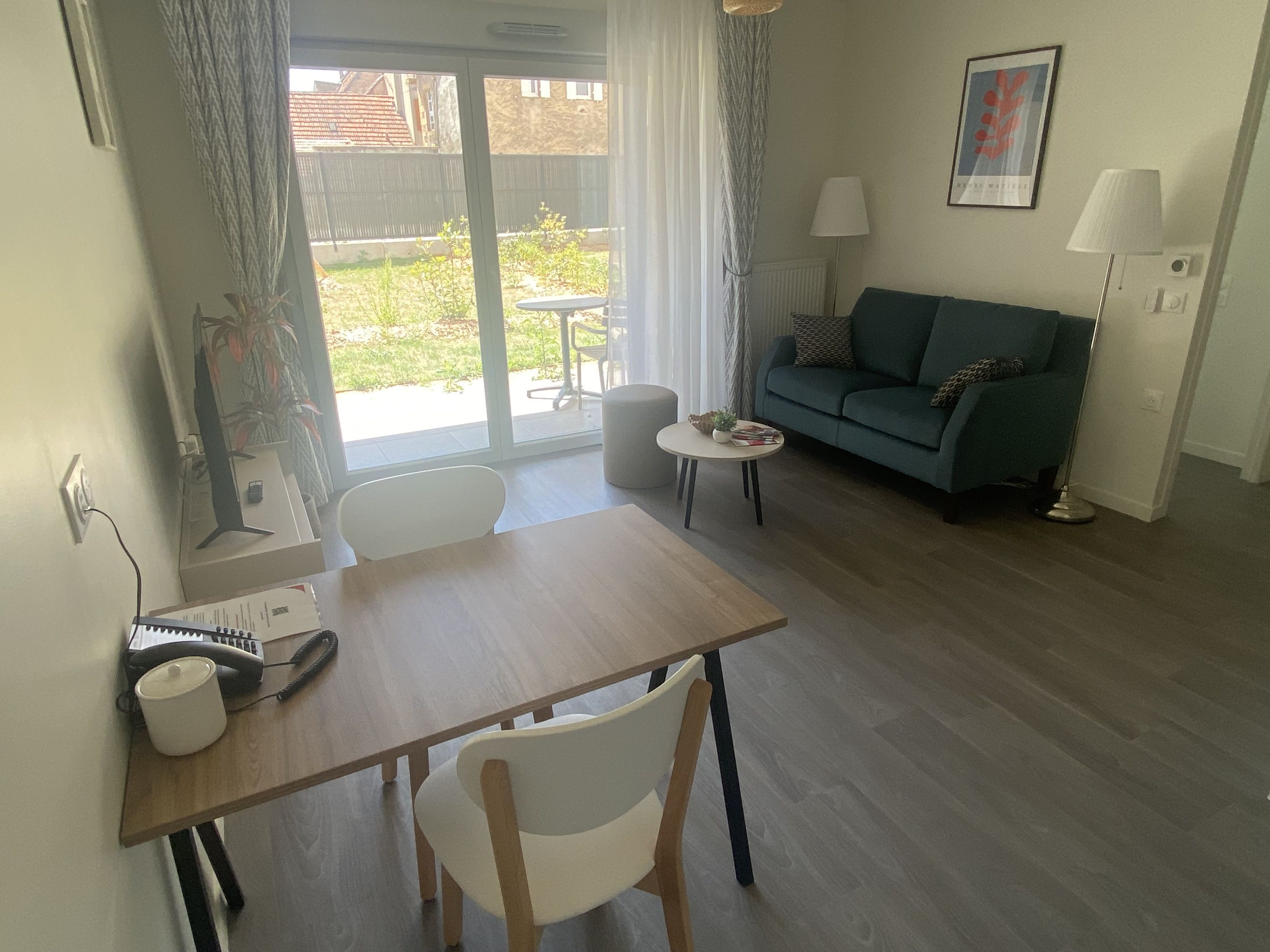 Un salon avec une table en bois, des chaises blanches, un canapé vert, une petite table ronde et une lampe.