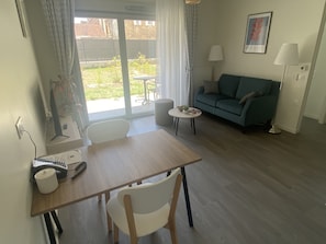 A living room with a wooden table, white chairs, a green sofa, a small round table, and a lamp.