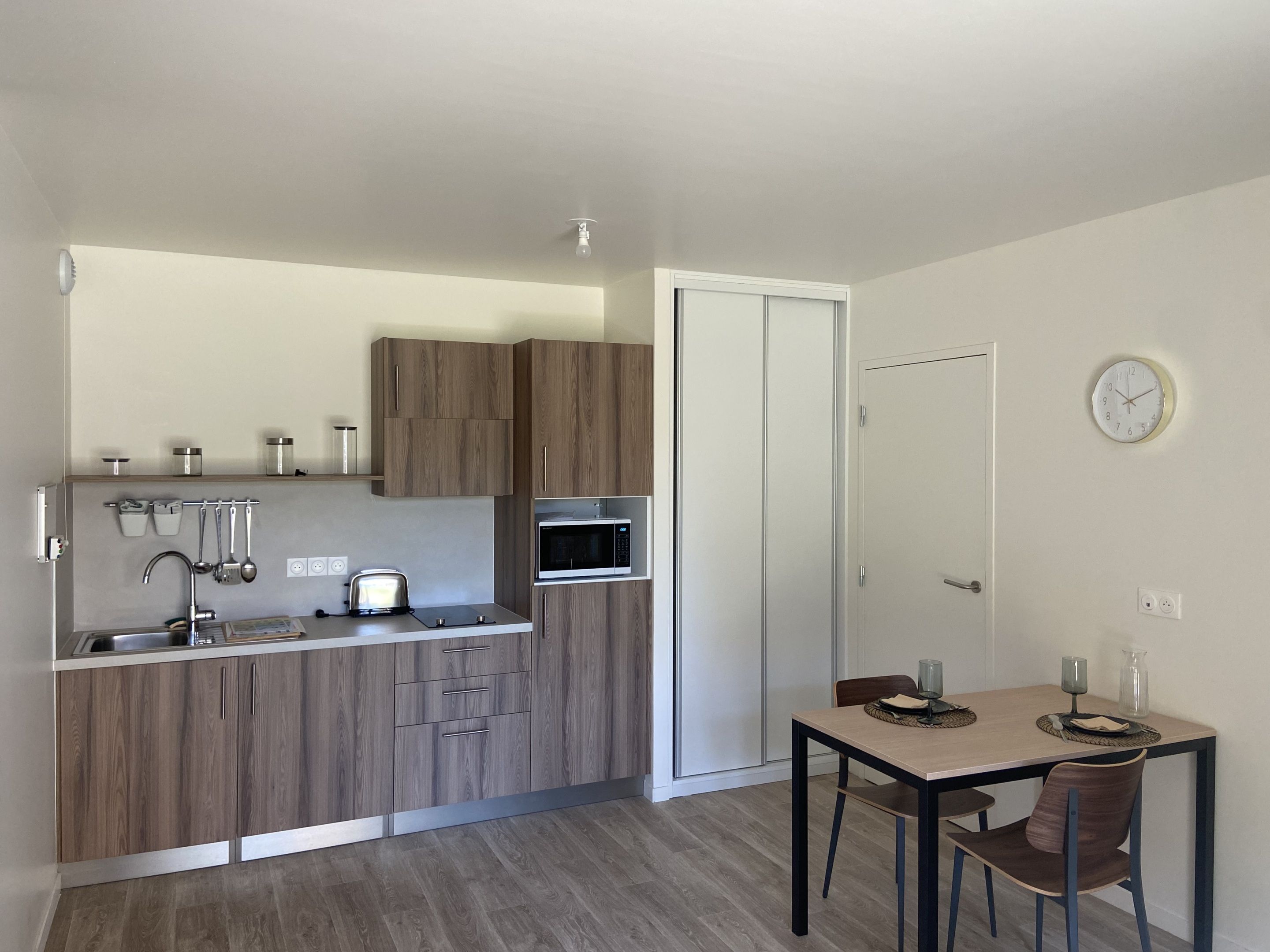Uma cozinha compacta com armários de madeira, micro-ondas, torradeira e uma área de refeições com mesa e cadeiras.