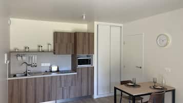 Uma cozinha compacta com armários de madeira, micro-ondas, torradeira e uma área de refeições com mesa e cadeiras.