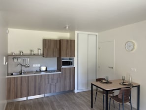 A compact kitchen with wooden cabinets, a microwave, a toaster, and a dining area with a table and chairs.
