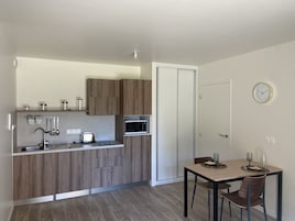 Cocina compacta con armarios de madera, microondas, tostadora y comedor con mesa y sillas.