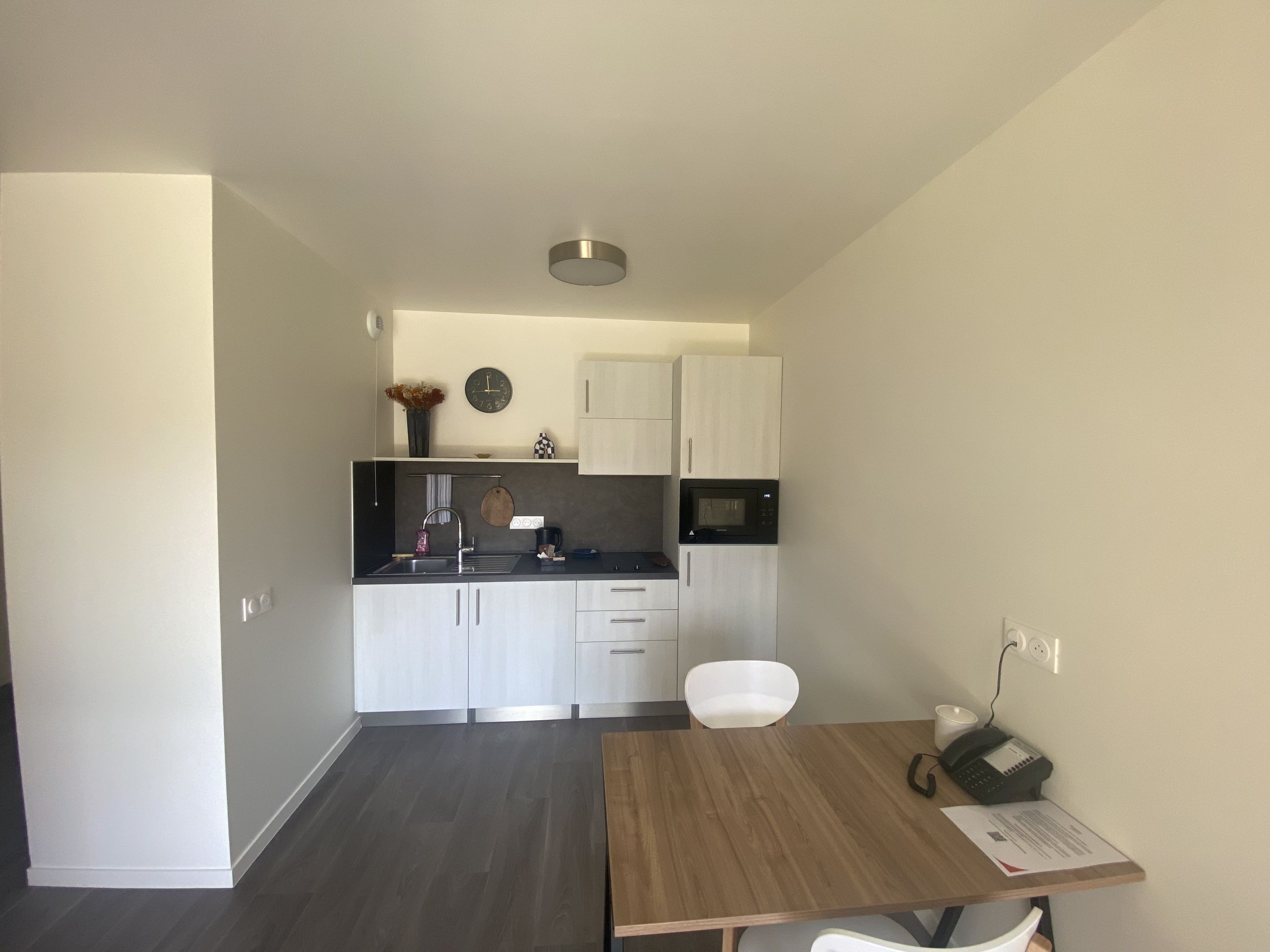 Une cuisine moderne avec des meubles blancs, un plan de travail noir et un four à micro-ondes. On y trouve une table à manger avec des chaises et un téléphone.