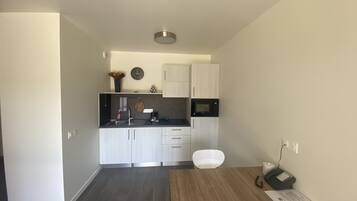 A modern kitchen with white cabinets, a black countertop, and a microwave. There is a dining table with chairs and a telephone.