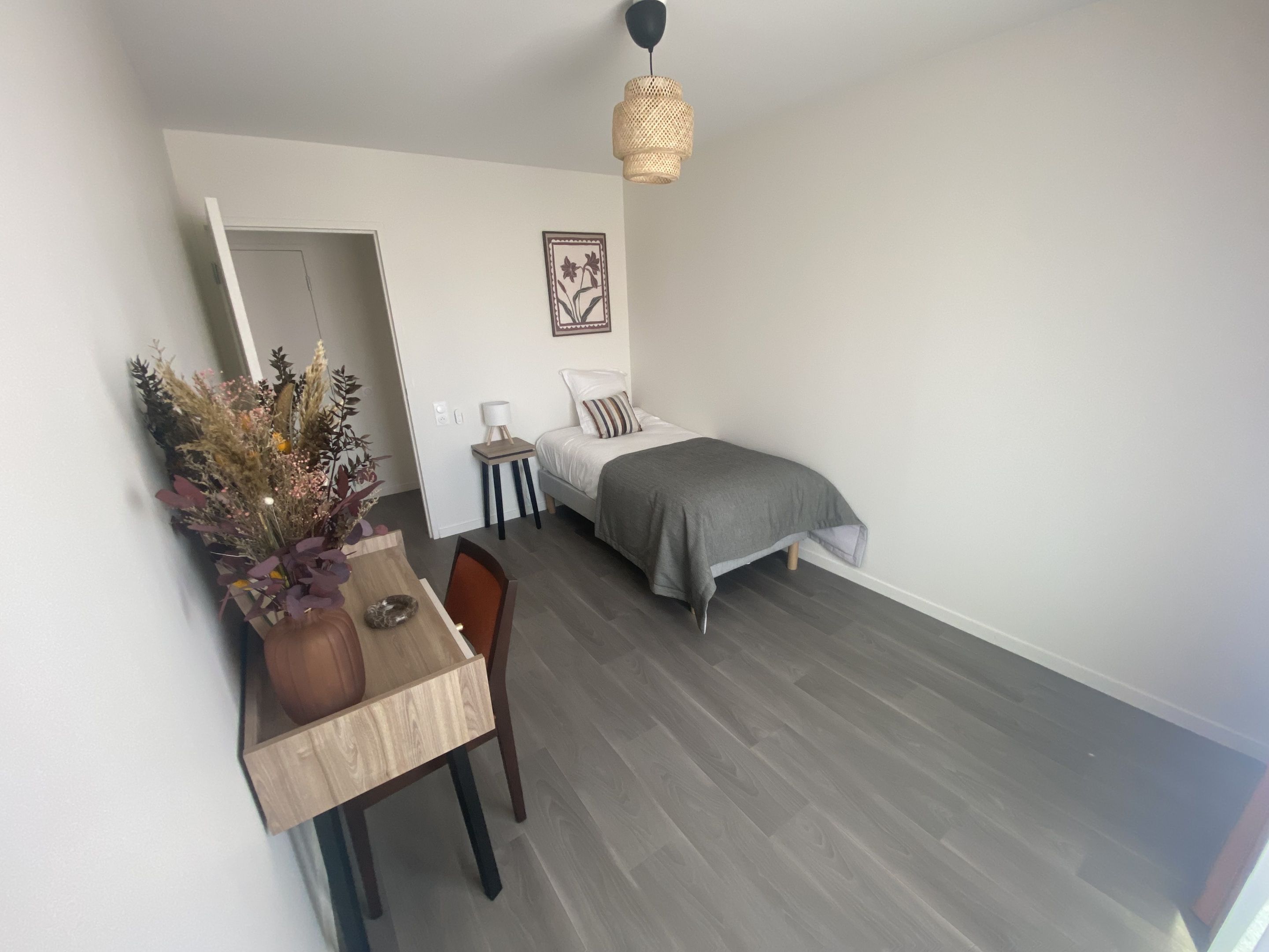 Un dormitorio pequeño y moderno con cama, mesita de noche, lámpara y un adorno en la pared.