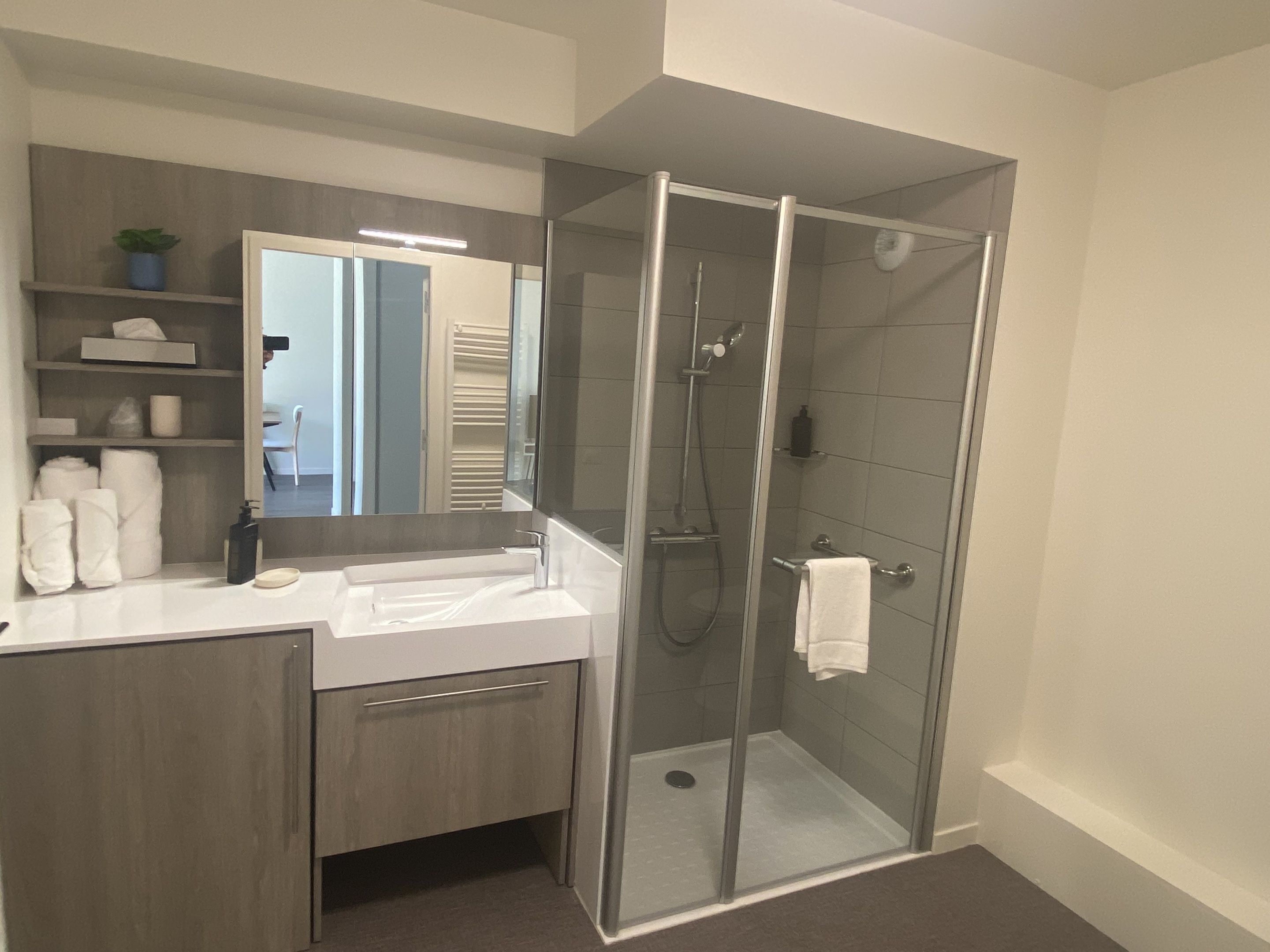 Un baño moderno con ducha de vidrio, tocador con espejo y un perchero para toallas.