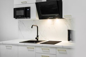 Une cuisine moderne avec un micro-ondes noir, une hotte noire, un évier avec un robinet noir et un pare-feu en marbre.