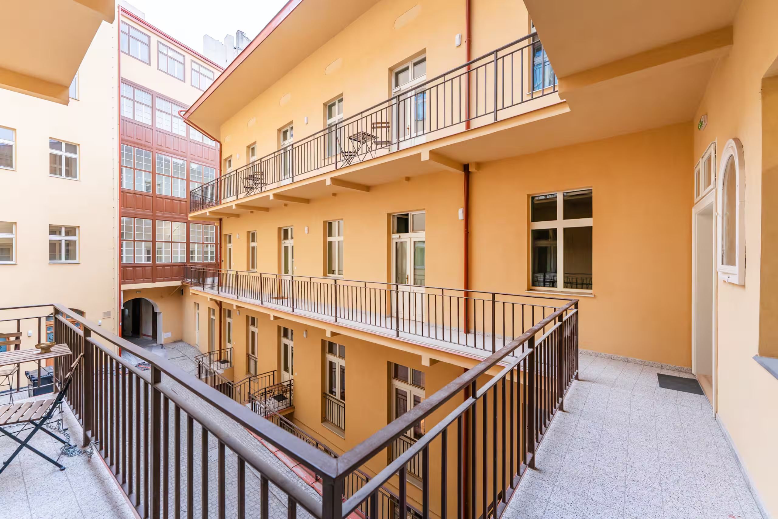 A multi-story building with balconies, a covered outdoor seating area, and a tiled ground floor.