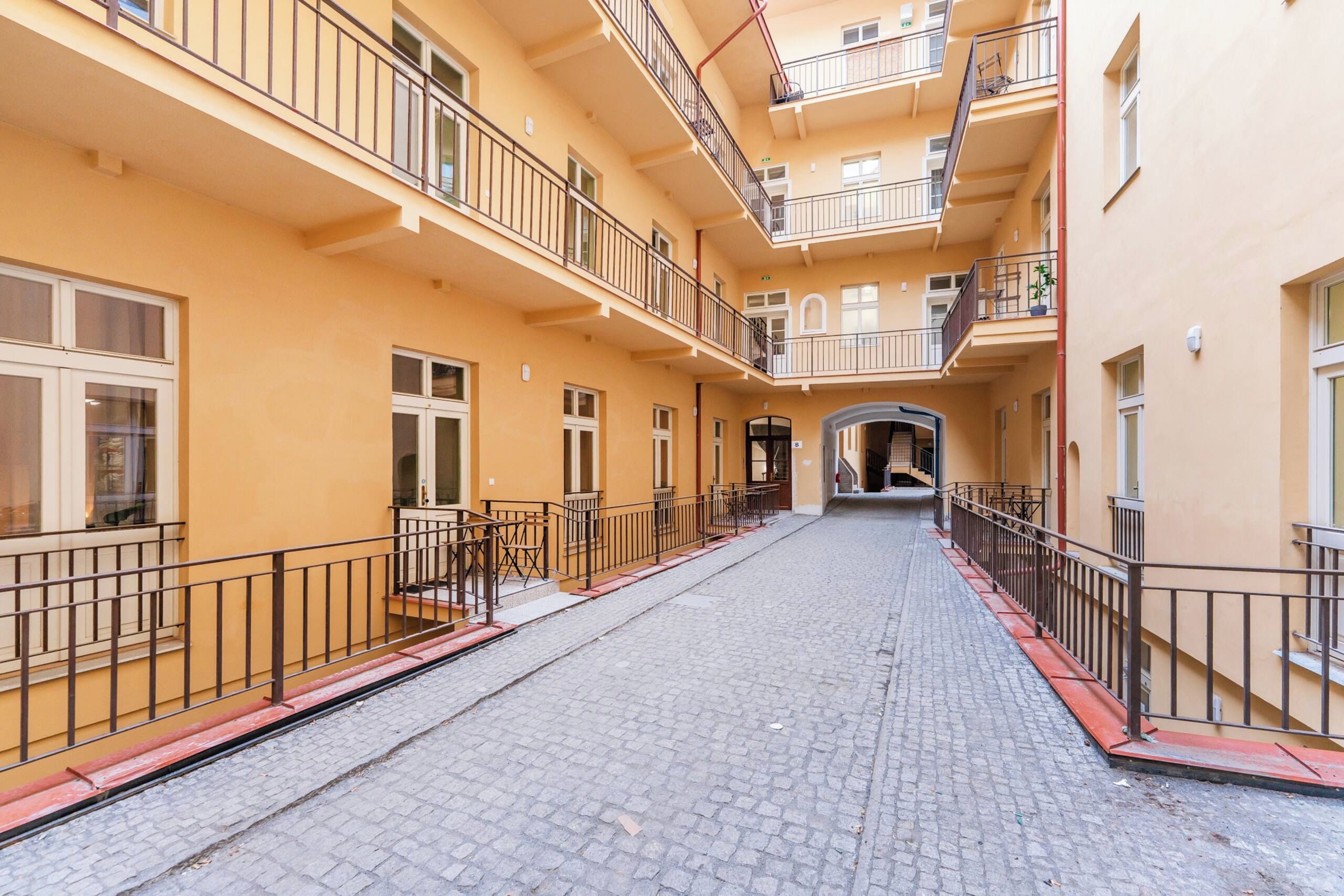 A multi-story building with balconies, a cobblestone street, and a central archway.