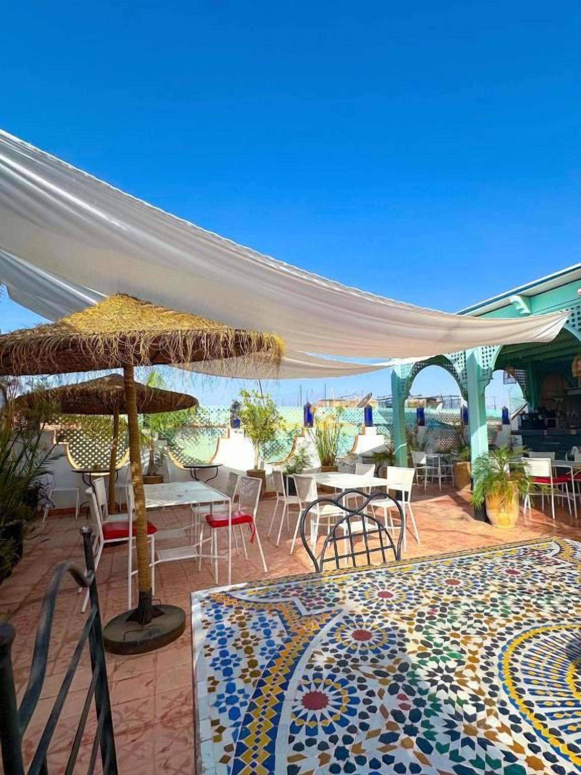 Un patio exterior con mesas y sillas, piso estampado y un toldo.