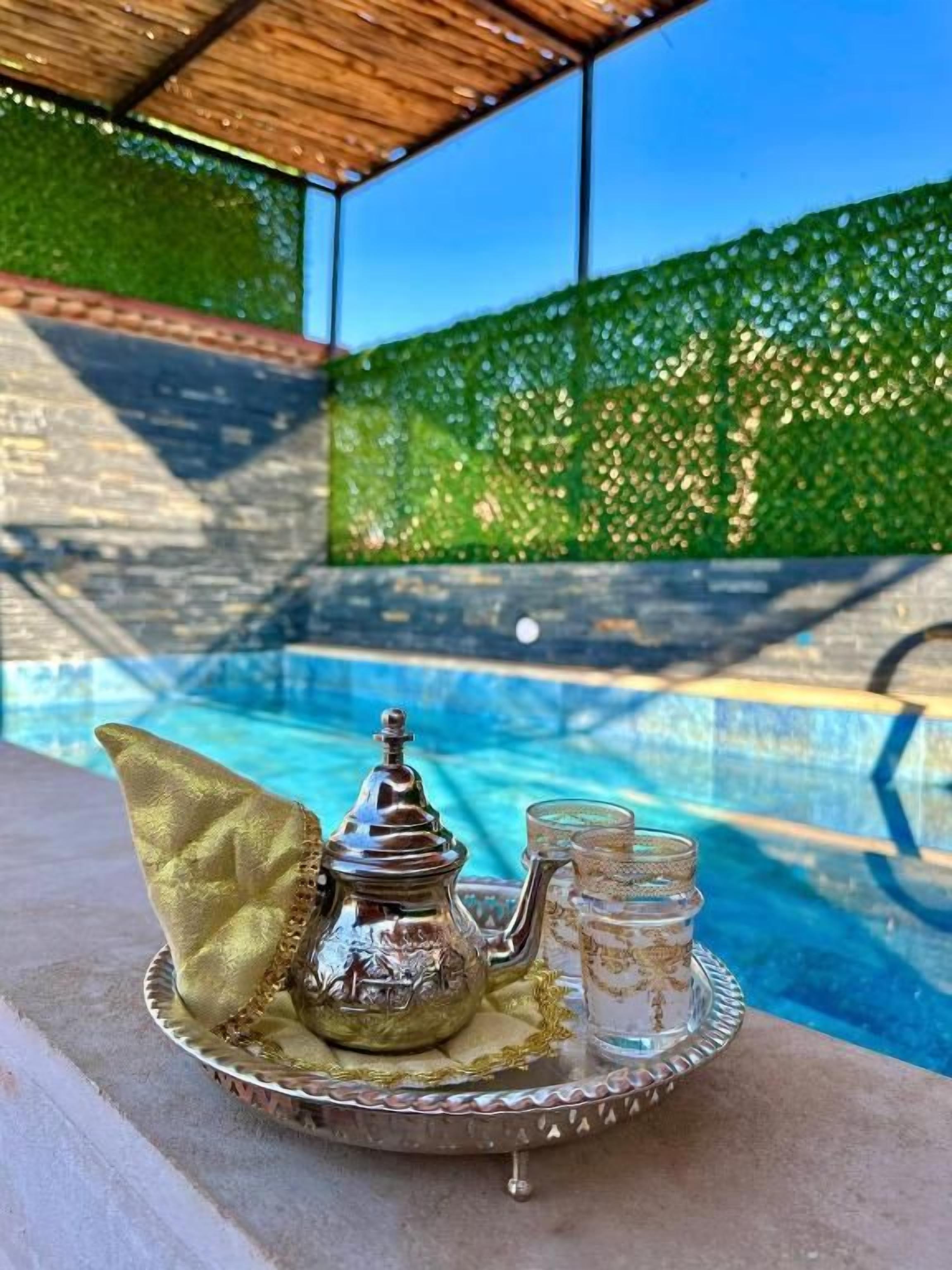 A tray with a teapot and glasses on a poolside area with a clear view of the pool.