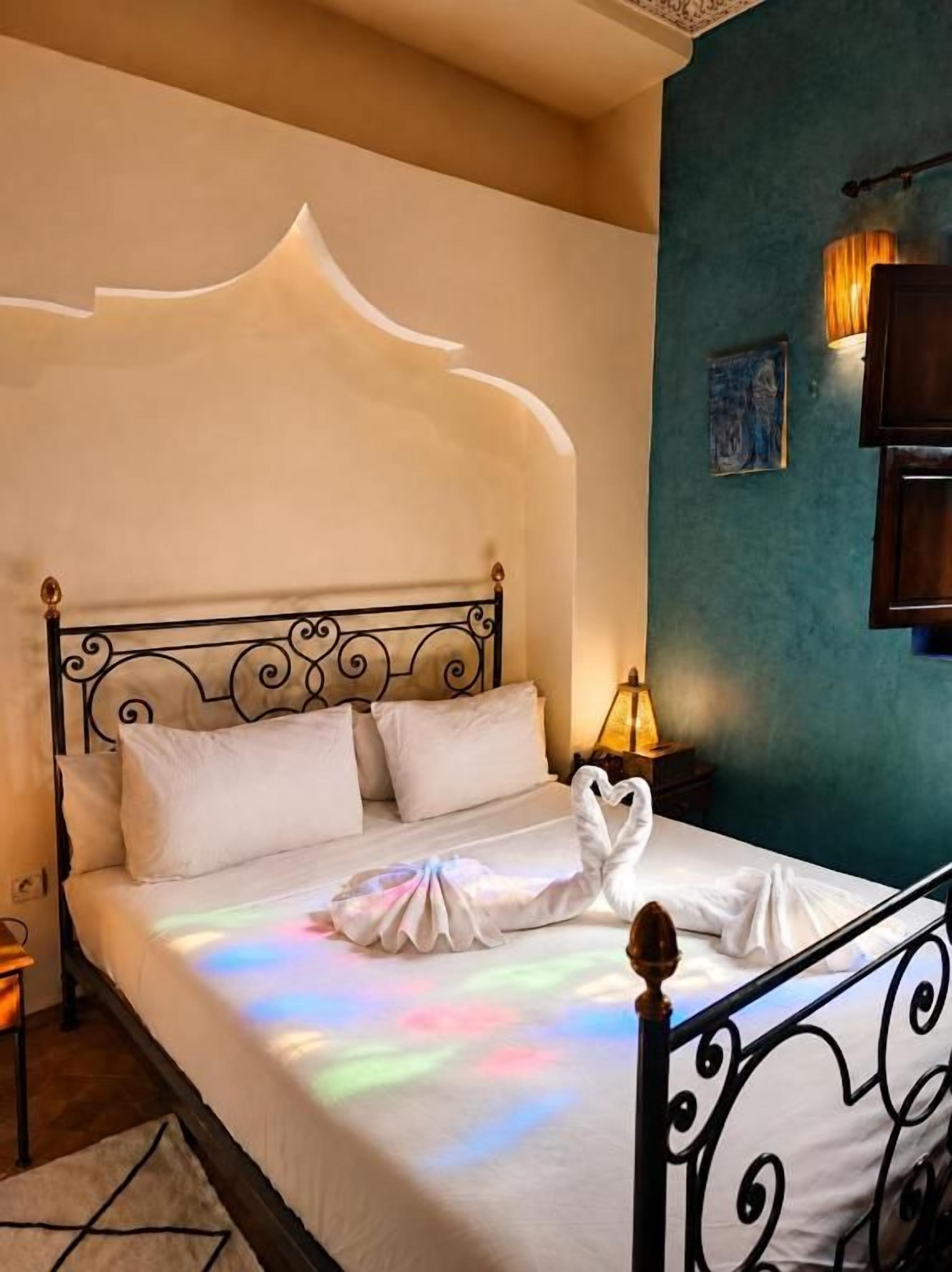 A bed with a decorative headboard, white linens, and a swan-shaped pillow.