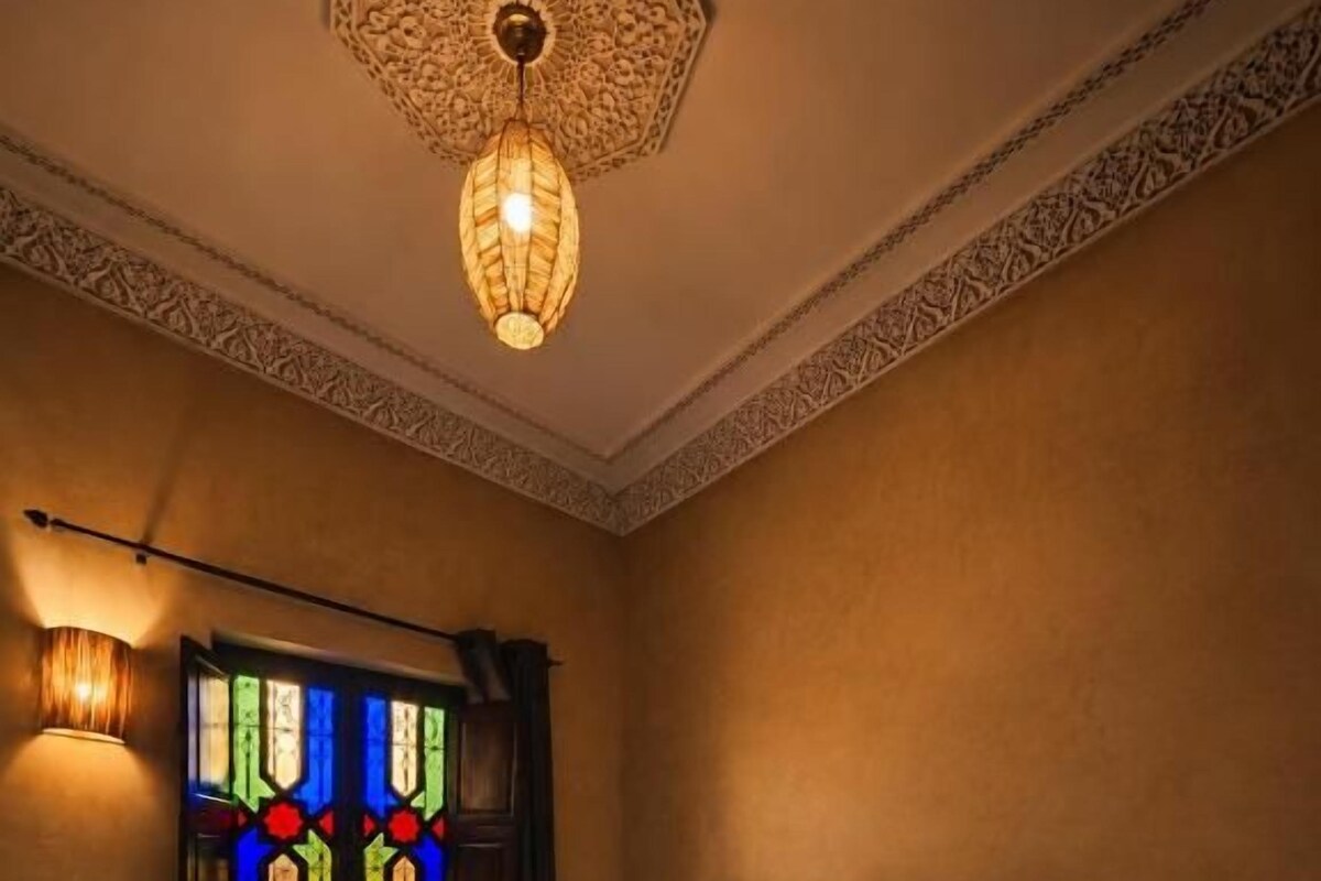 Et hotelværelse med en stor seng, en dekorativ loftlampe, et farvet glasvindue og en sengetavlelampe.
