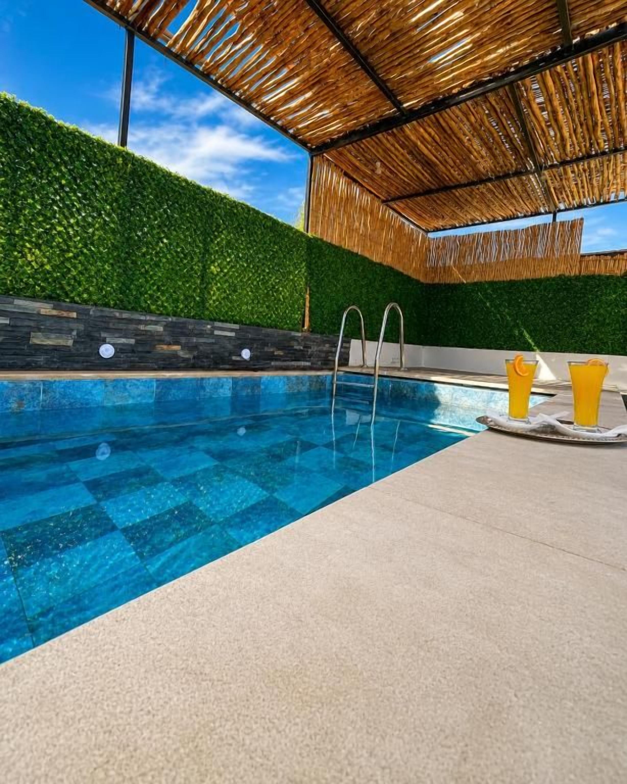 Una piscina con superficie de agua azul cristalina, rodeada por una terraza de concreto y un techo de paja.