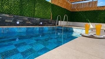 Una piscina con superficie de agua azul cristalina, rodeada por una terraza de concreto y un techo de paja.
