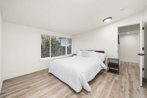 Ein Schlafzimmer mit einem Bett, einem Nachttisch, einem Fenster mit Jalousien und einer Tür.