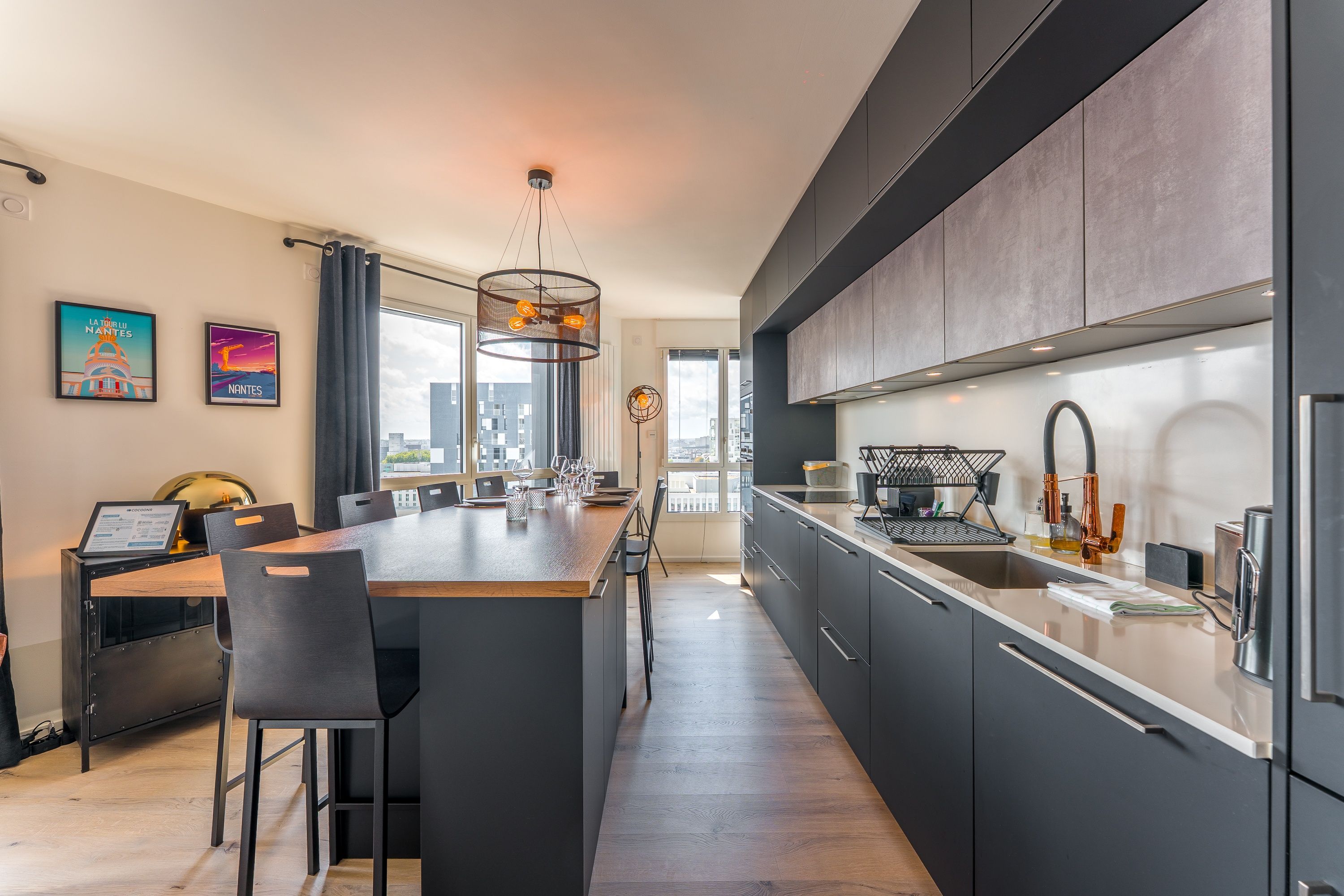 A modern kitchen with a large island, dark cabinetry, and a view of the city.