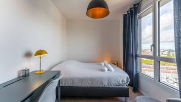 Een hotelkamer met een bed, een bureau, een lamp en uitzicht op de stad.