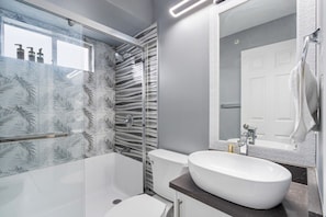 Un baño moderno con cabina de ducha de vidrio, un lavabo blanco y un espejo grande.