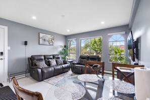 A modern living room with a grey sofa set, a glass coffee table, and a flat-screen TV mounted on the wall.