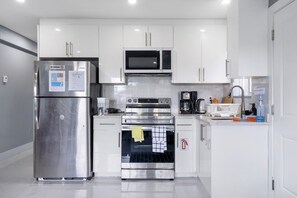 A modern kitchen with stainless steel appliances, white cabinetry, and a tiled backsplash.