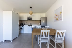A modern kitchen with white cabinetry, a wooden dining table, and a hanging light fixture. - Masade - cocon avec piscine partagée (Trans-en-Provence)