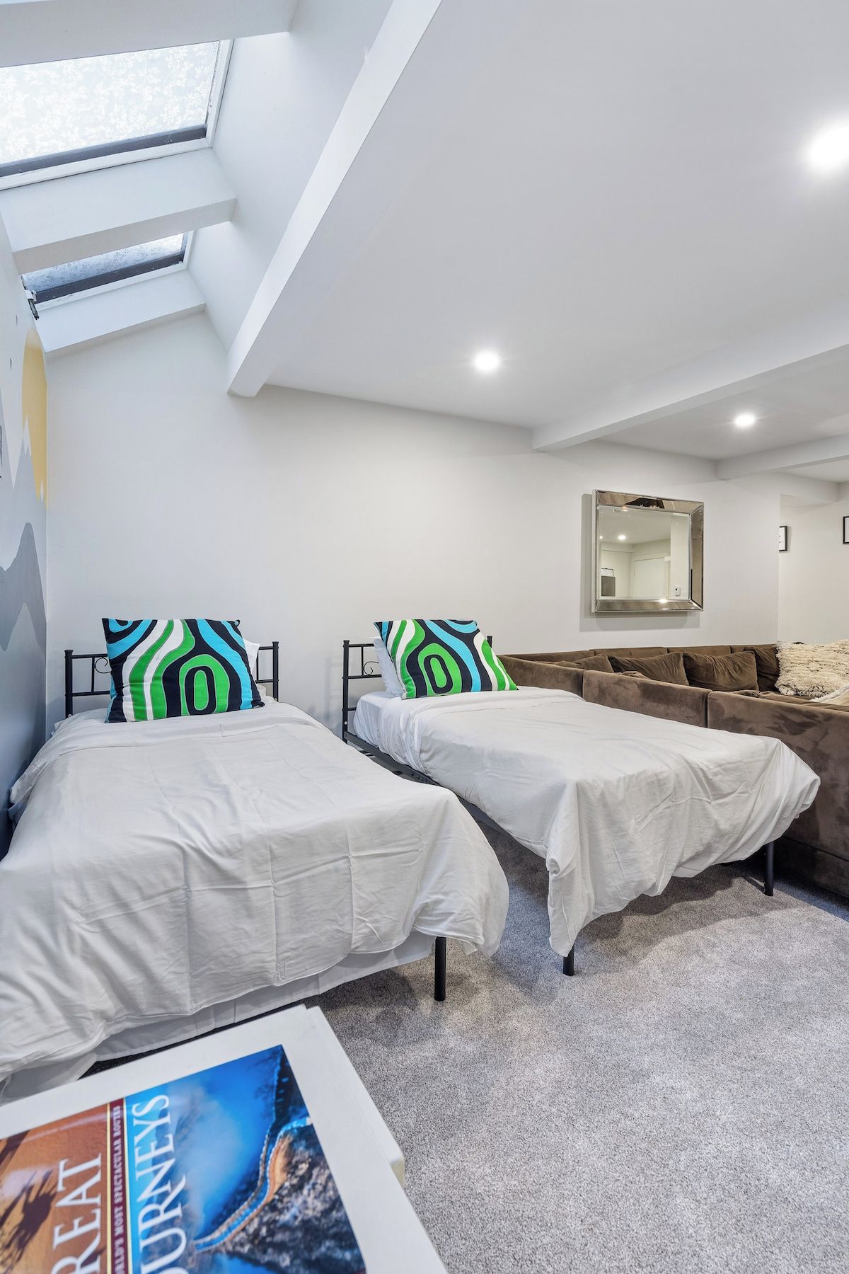 A modern bedroom with two single beds, a sofa, a skylight, and a large mirror.