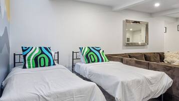 A modern bedroom with two single beds, a sofa, a skylight, and a large mirror.