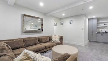 Uma sala de estar moderna com um sofá marrom, um banquinho redondo e um espelho grande na parede.