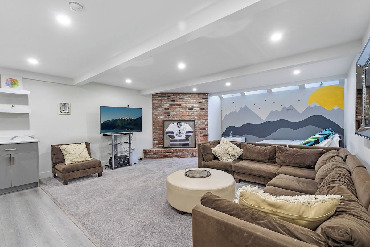 A modern living room with a flat-screen TV, a brick fireplace, and a mural on the wall.