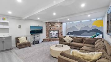 A modern living room with a flat-screen TV, a brick fireplace, and a mural on the wall.