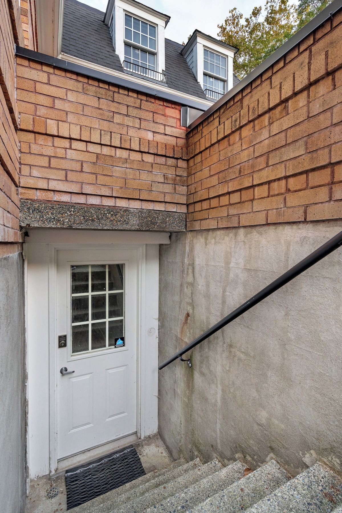 A white door with a window, a brick wall, and a concrete staircase.
