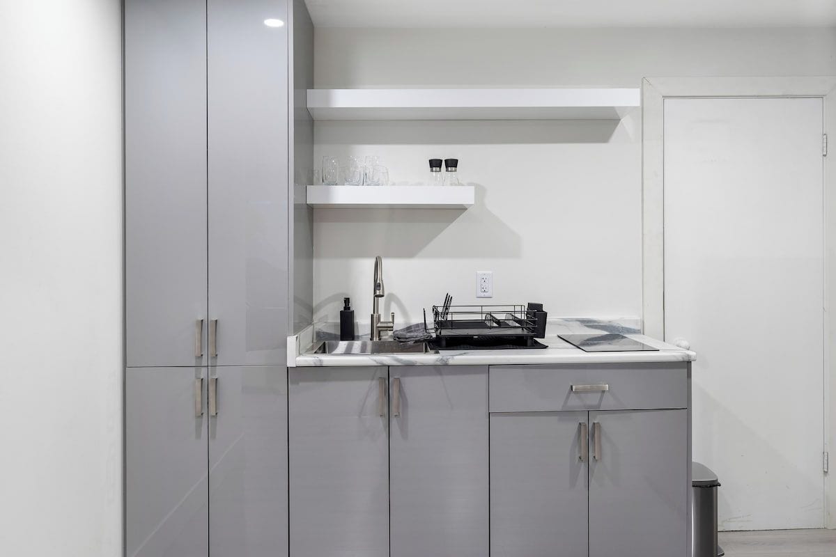 A modern kitchen with a built-in dishwasher, a countertop with a sink, and a white shelf above the sink.
