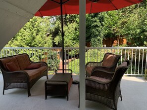 Ein überdachter Patio-Bereich mit Korbmöbeln, darunter zwei Sofas und eine Bank, unter einem roten Sonnenschirm.