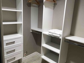Ein begehbarer Kleiderschrank mit offenen Regalen, einer Kleiderstange und einem gefalteten Handtuch auf einem der Regale.
