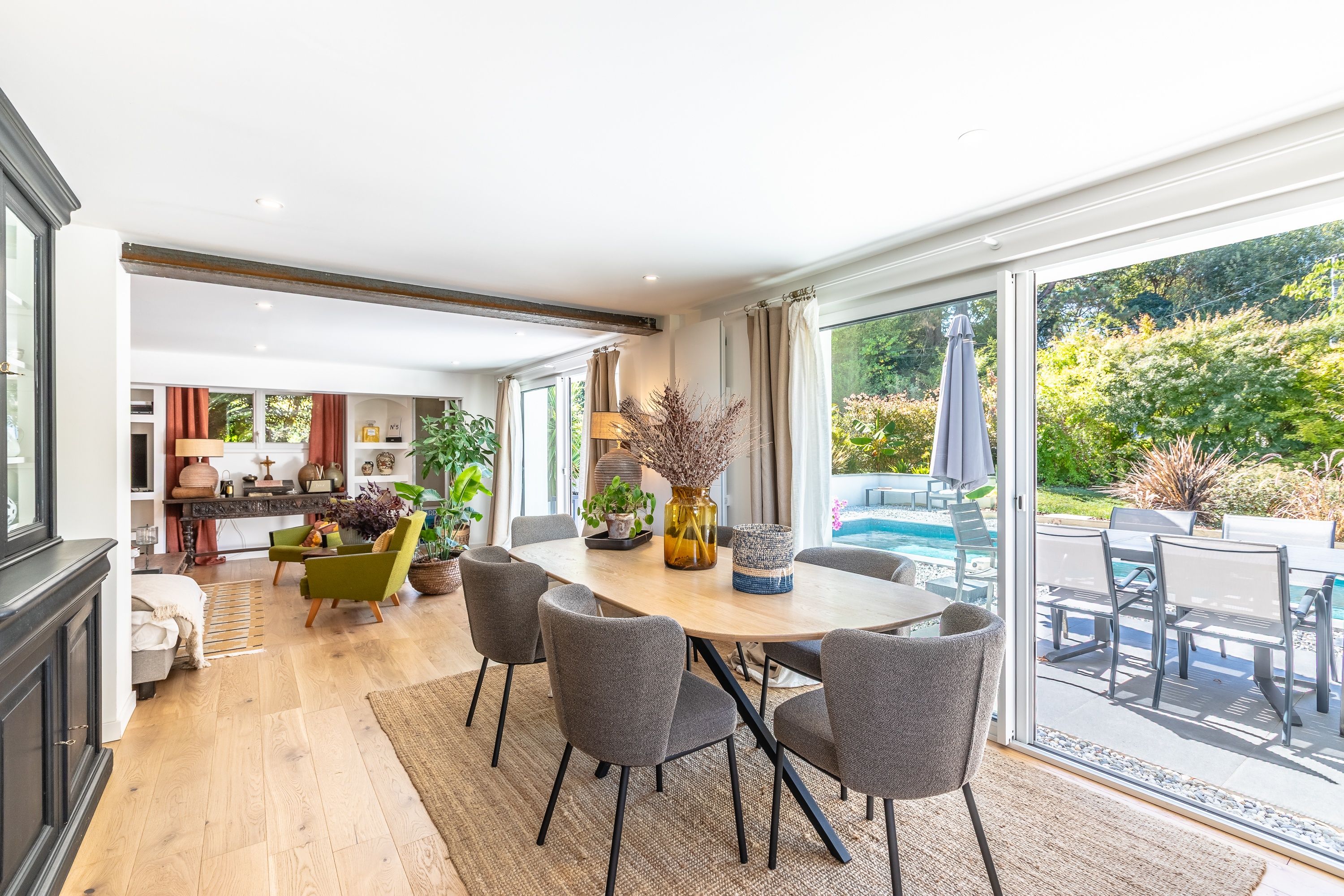 A spacious dining area with a large table and chairs, a view of a swimming pool, and a kitchen in the background.