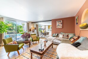 A spacious living area with a sofa, armchairs, and a dining table. There is a large window providing a view of the outdoors. - Villa Gabrielle - rez-de-jardin, piscine privée (Bassussarry)