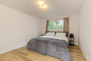 A bedroom with a bed, a window with curtains, a bedside table, and a wall-mounted light fixture. - Relaxing Lynnwood Getaway | Two Beds with Parking (Lynnwood)