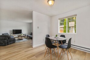 A modern living room with a flat-screen TV, a sofa, and a dining area with a table and chairs. - Relaxing Lynnwood Getaway | Two Beds with Parking (Lynnwood)