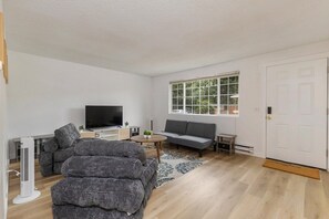 A modern living room with a flat-screen TV, grey sofas, a coffee table, and a large window. - Relaxing Lynnwood Getaway | Two Beds with Parking (Lynnwood)