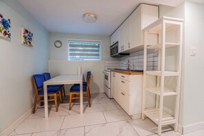 A compact kitchen with a dining table, chairs, a microwave, and a white shelving unit.