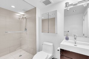 Ein modernes Badezimmer mit einer Duschkabine aus Glas, einer weißen Toilette, einem Waschbecken mit Spiegel und einer Seifenflasche.